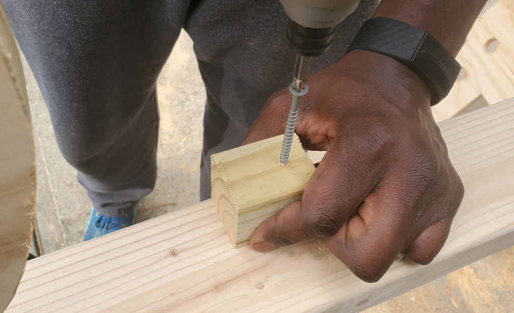 A person drilling a small block into a 2 x 4 board.