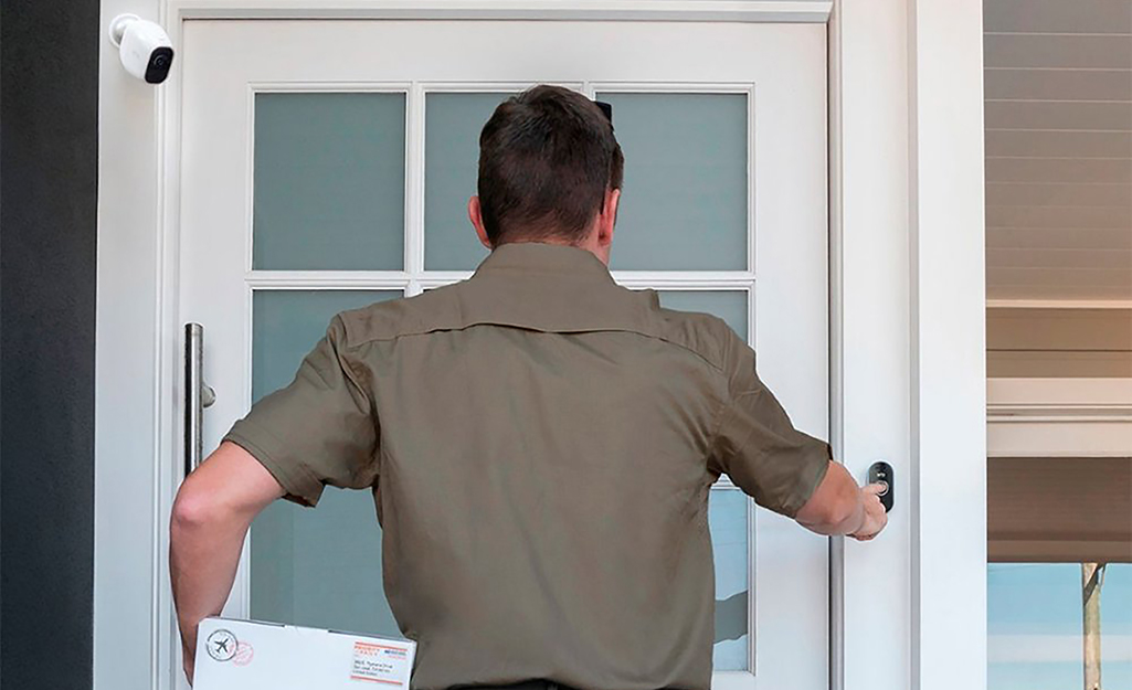 A person ringing a front door bell in view of a security camera.