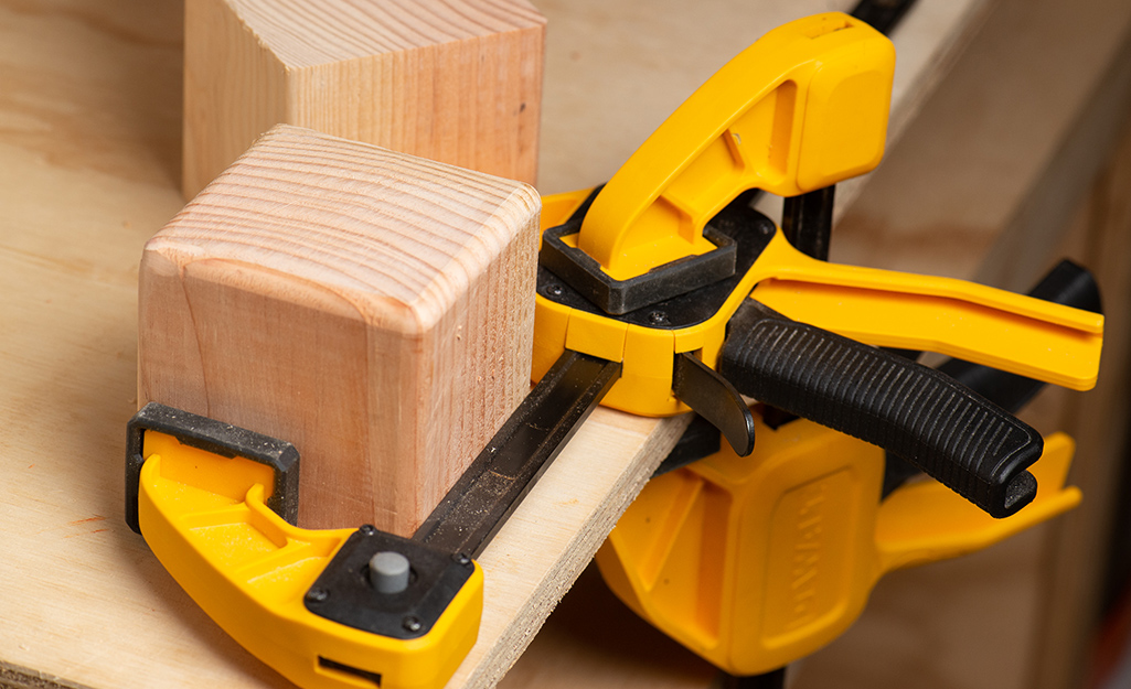 A wooden cube secured on a worktable by clamps.