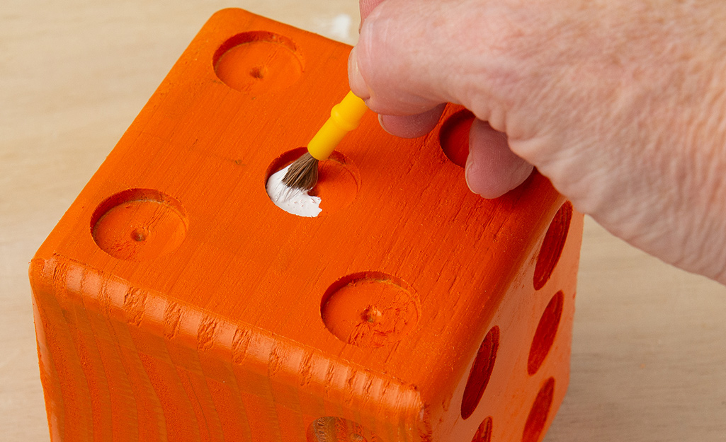 A person painting the wooden die.