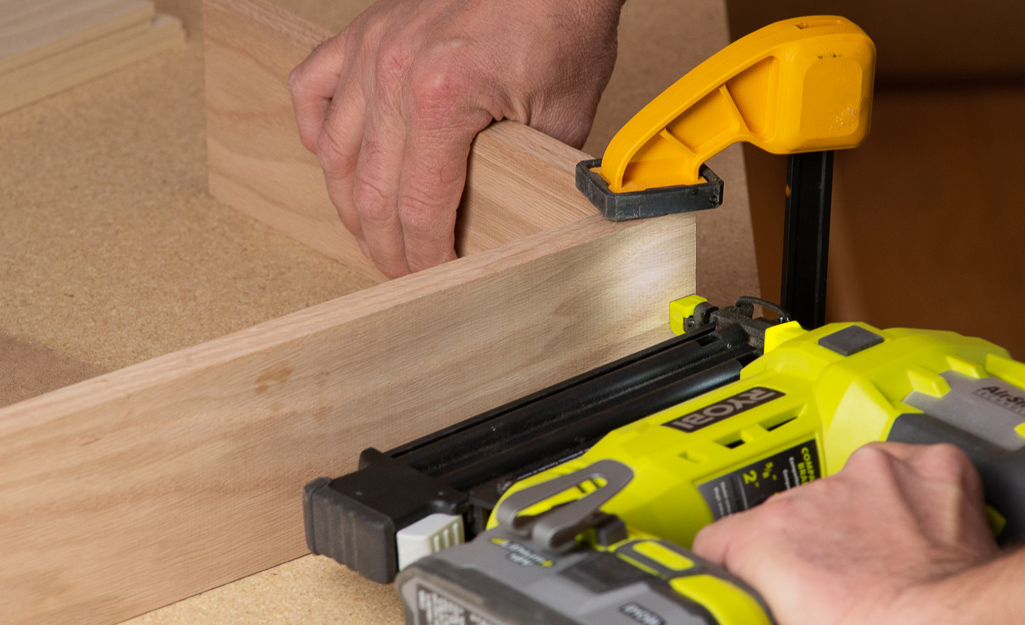 A person using a brad nailer to fasten a box together. A person using a brad nailer to fasten a box together.