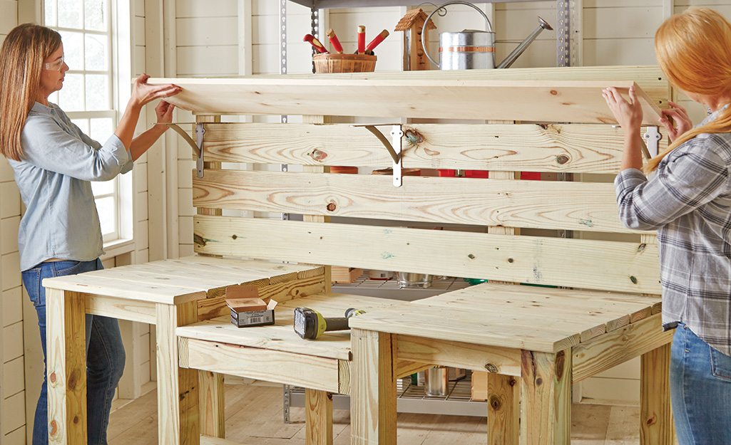 Two people adding a wood shelf to the top of the potting bench.