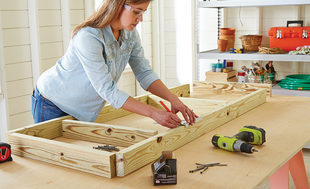 A person marking the lower shelf frame of a potting bench.