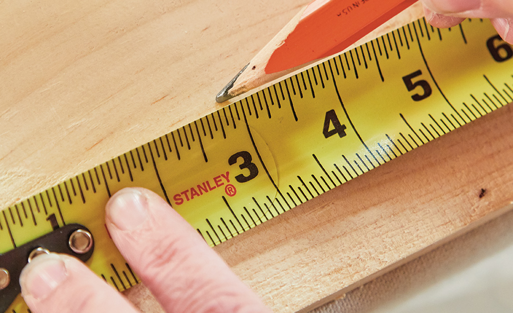 A person uses a tape measure to measure wood. A person uses a tape measure to measure wood.