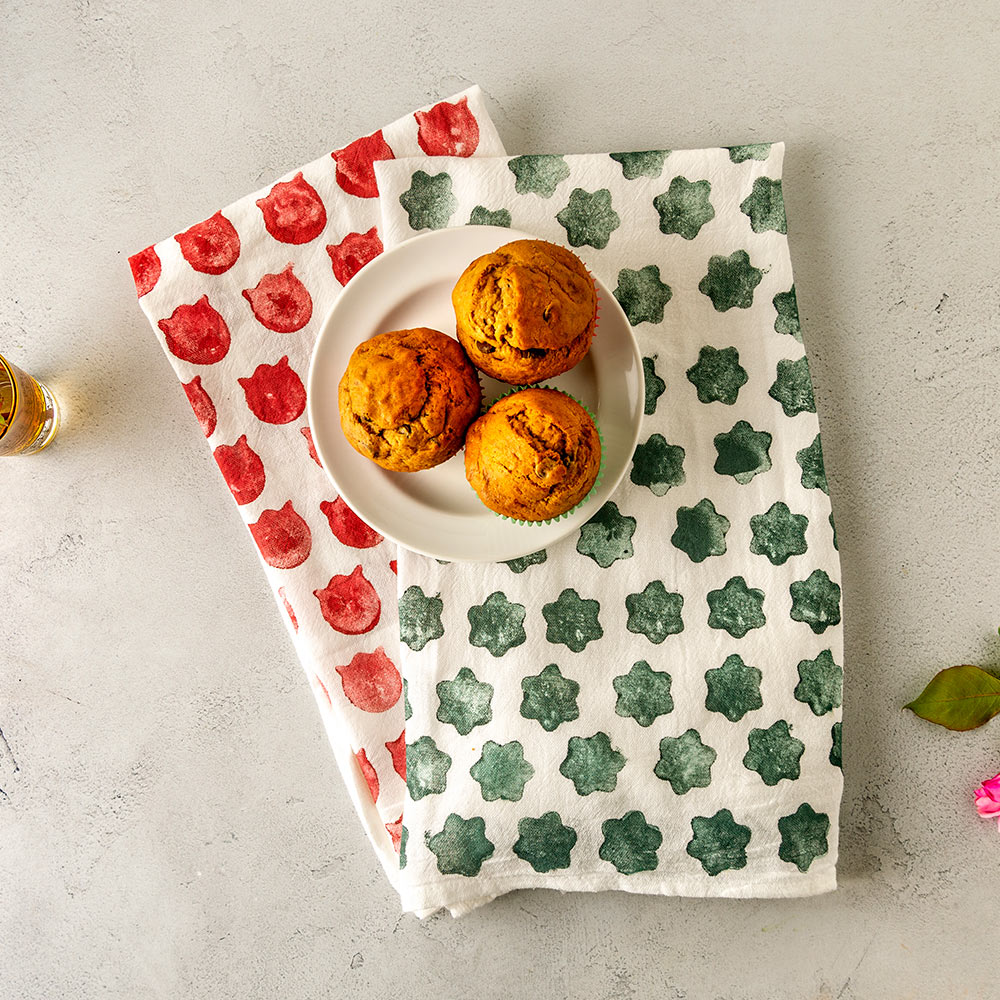Custom stamped tea towels lay on a table with a plate of muffins.