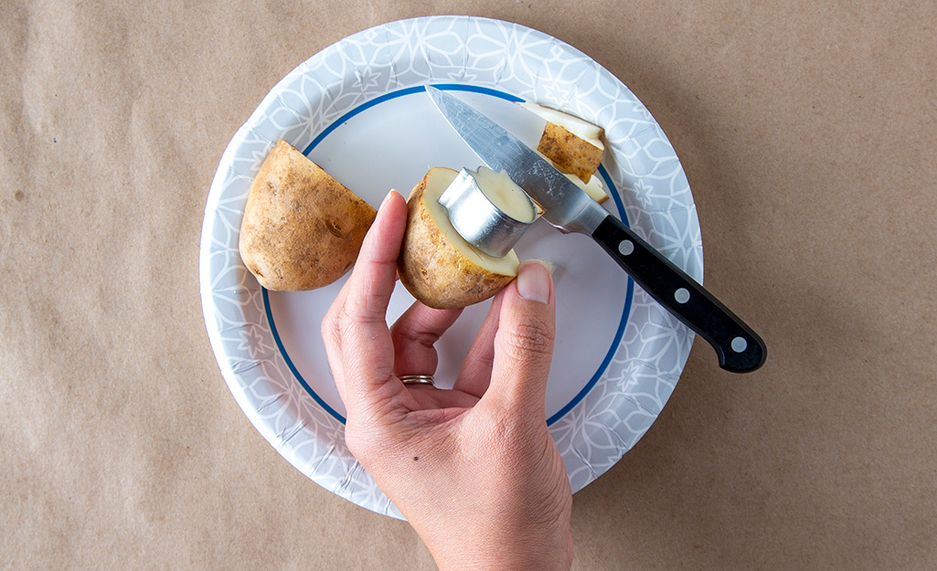 A person holds half of a potato with a cookie cutter shape carved into it to make a stamp.