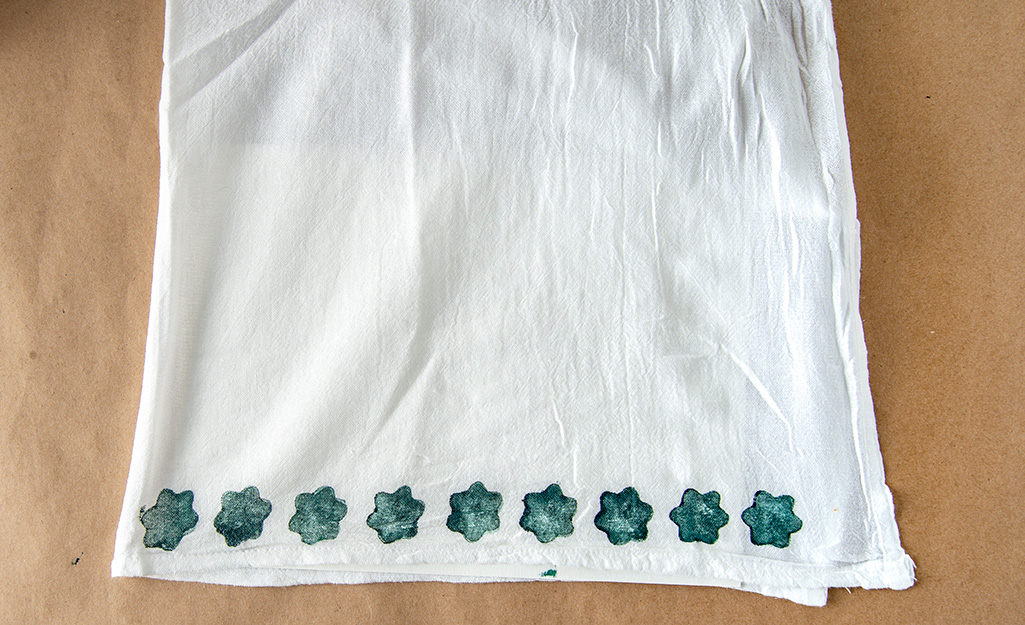 A row of green flowers has been stamped on the bottom edge of a white tea towel.
