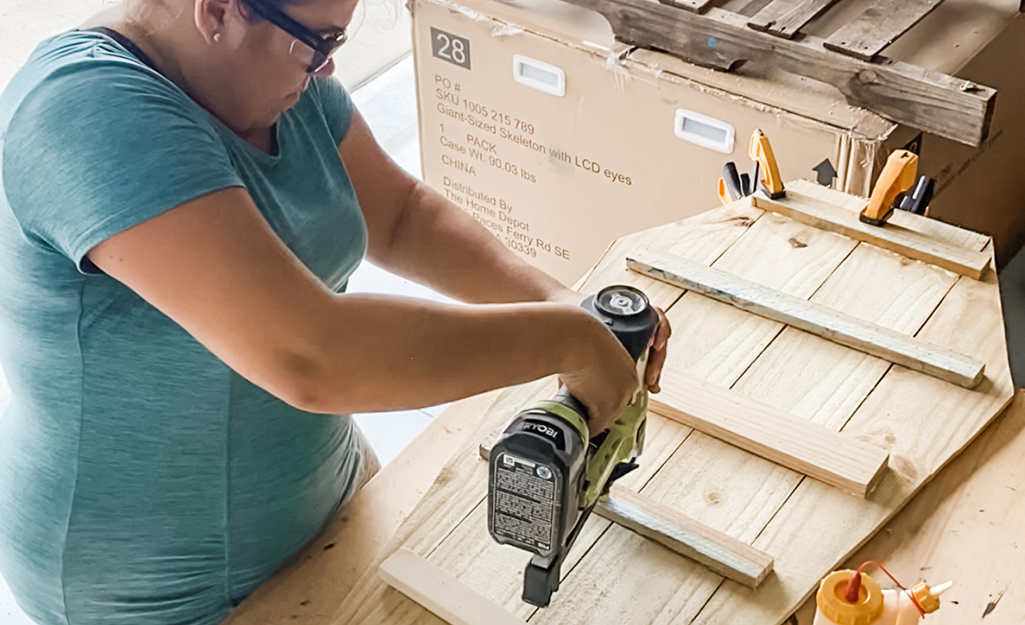 A woman uses a nail gun to secure braces to fence pickets.