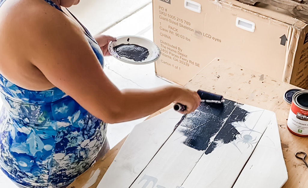 A woman uses a paint brush to apply black paint to fence pickets.