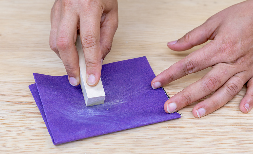 A person's hands sanding a dowel with sandpaper.