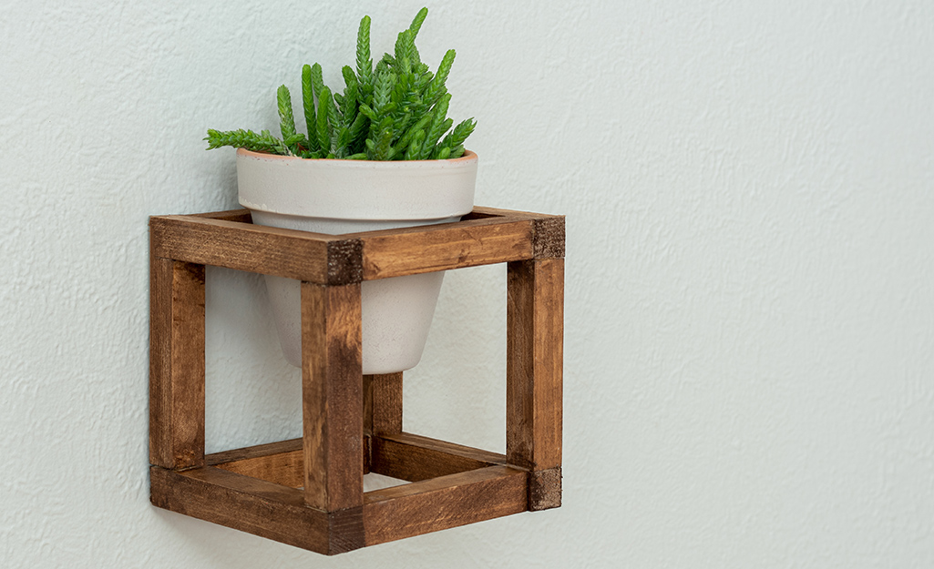 A potted plant in a freshly stained wooden plant hanger on a wall.