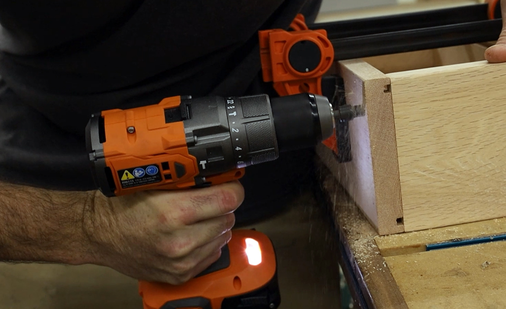 A person using a drill to screw wood boards together.