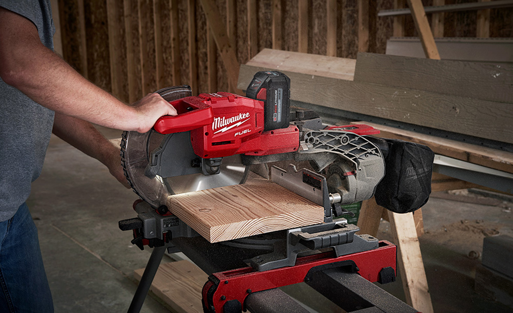 A person uses a miter saw to cut a piece of wood.