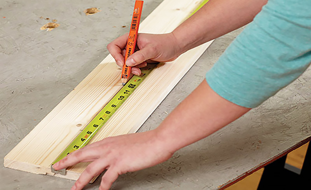 A person uses a tape measure and marker to measure a board length.