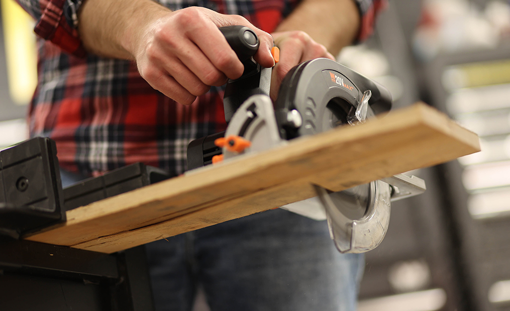 A person uses a circular saw to cut a wood board.