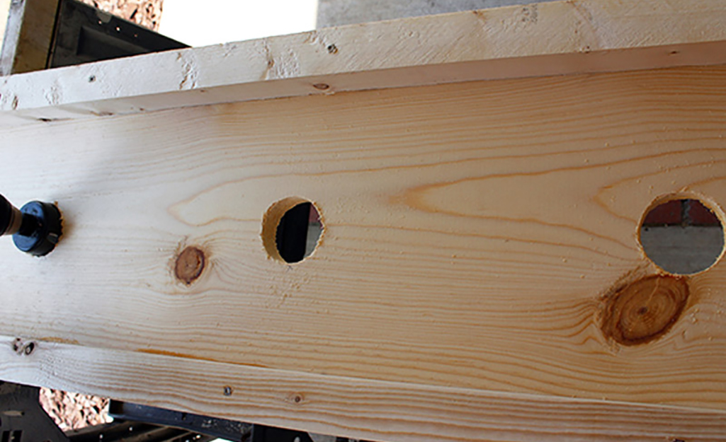 A person uses a hole saw to create draining holes in the window box.