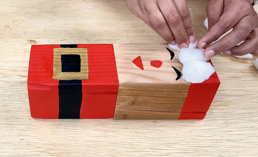 Cotton balls are glued to the block to form Santa's hat.