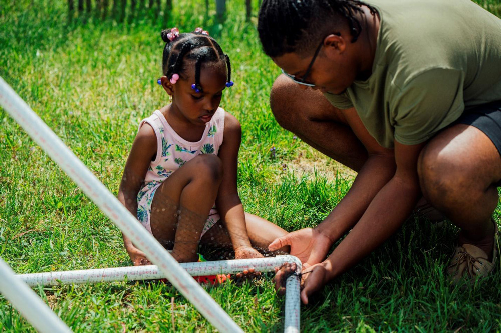 A man and little girl outside connecting PVC pipes together.