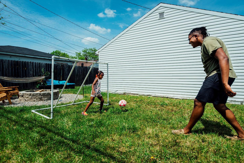 Man and girl in a backyard playing soccer.