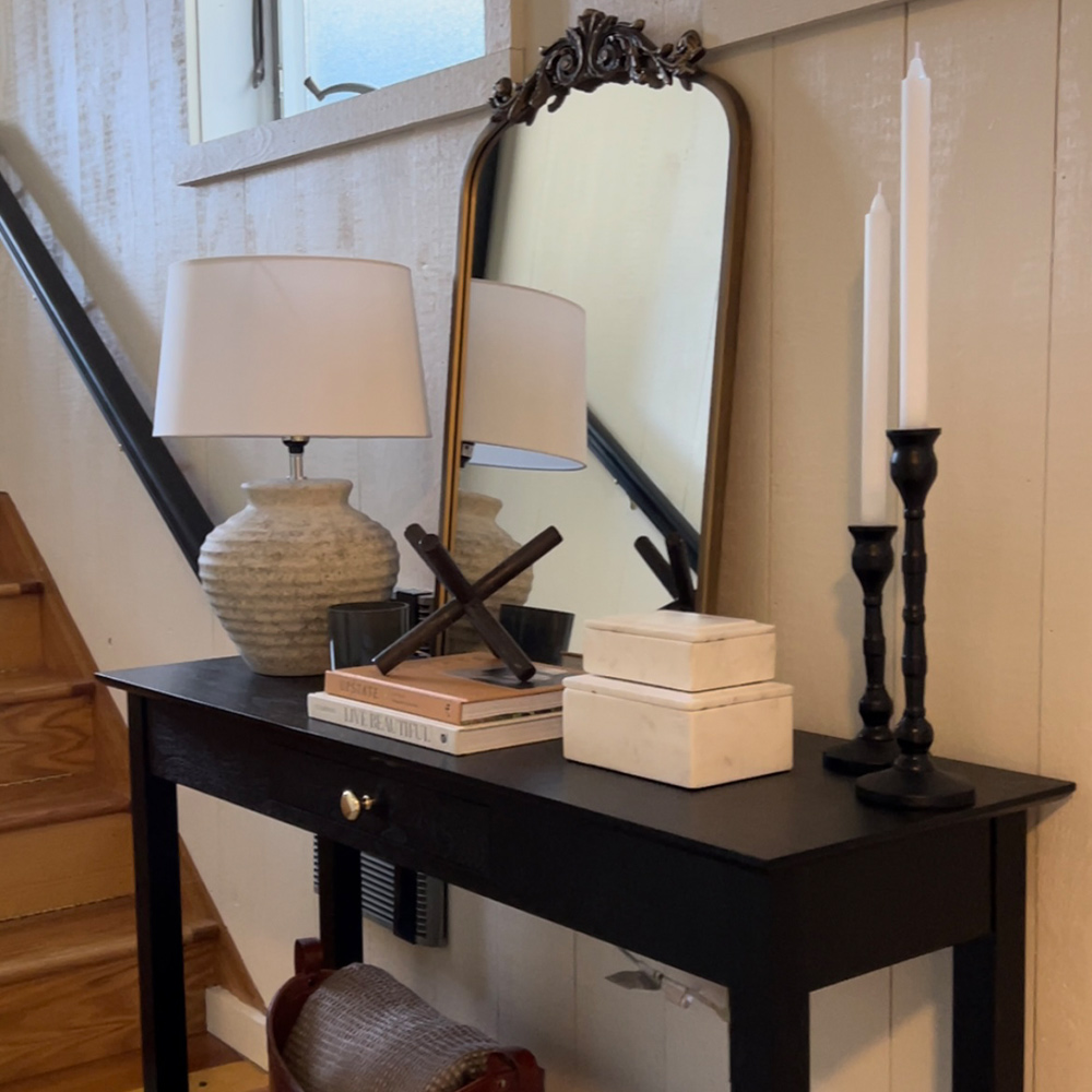 A hall table with a candle, lamp and a mirror.