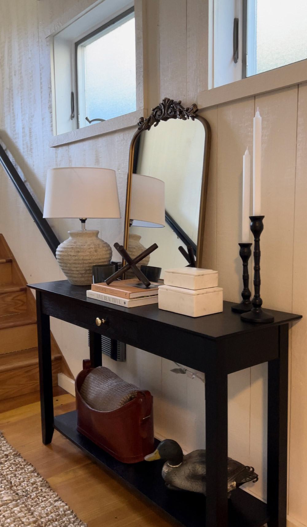 A hall table with a candle, lamp and a mirror.