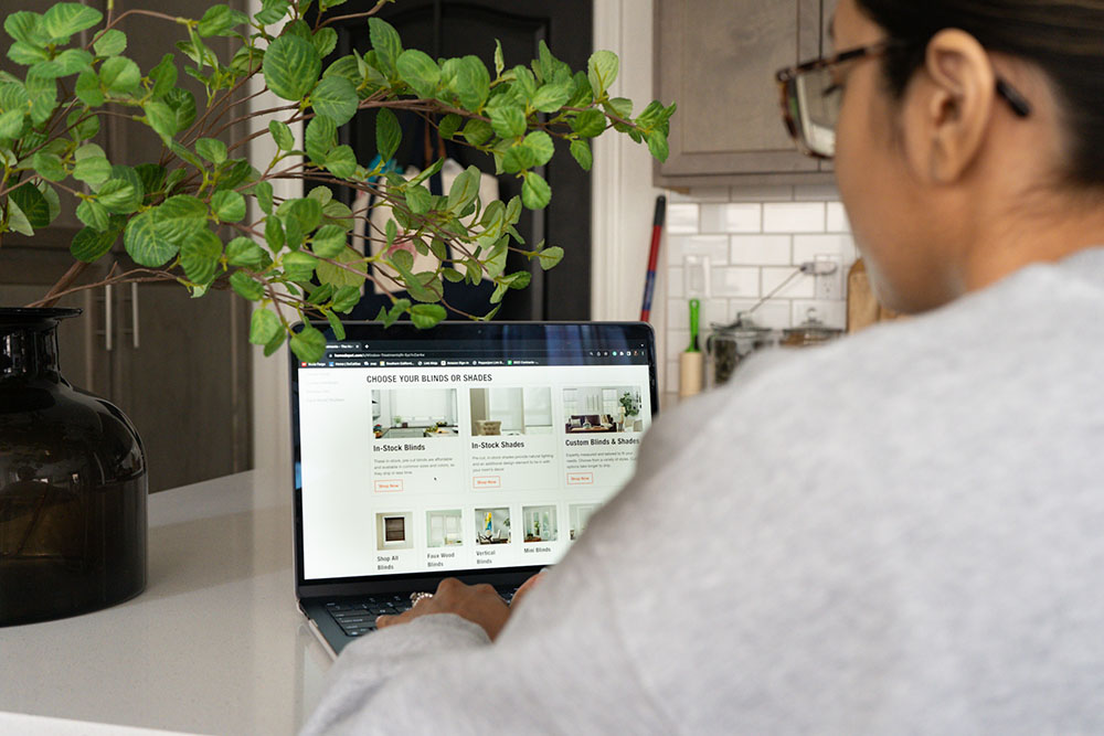 A woman on a computer over a white kitchen table with a green plant A woman on a computer over a white kitchen table with a green plant