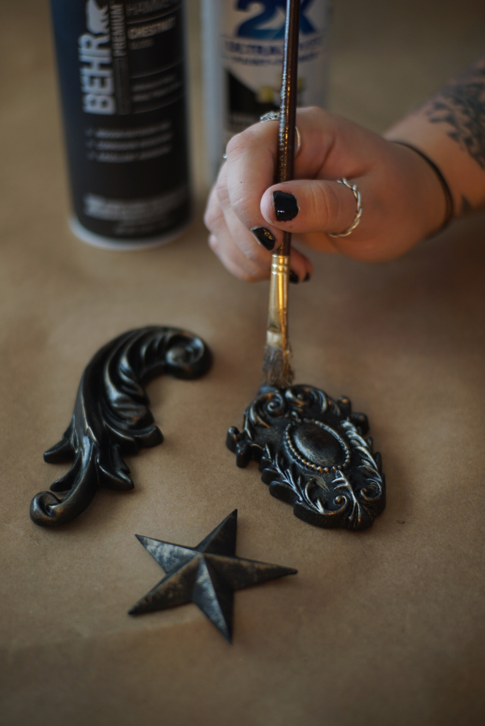 A person using a paintbrush to paint three moulding appliques black.
