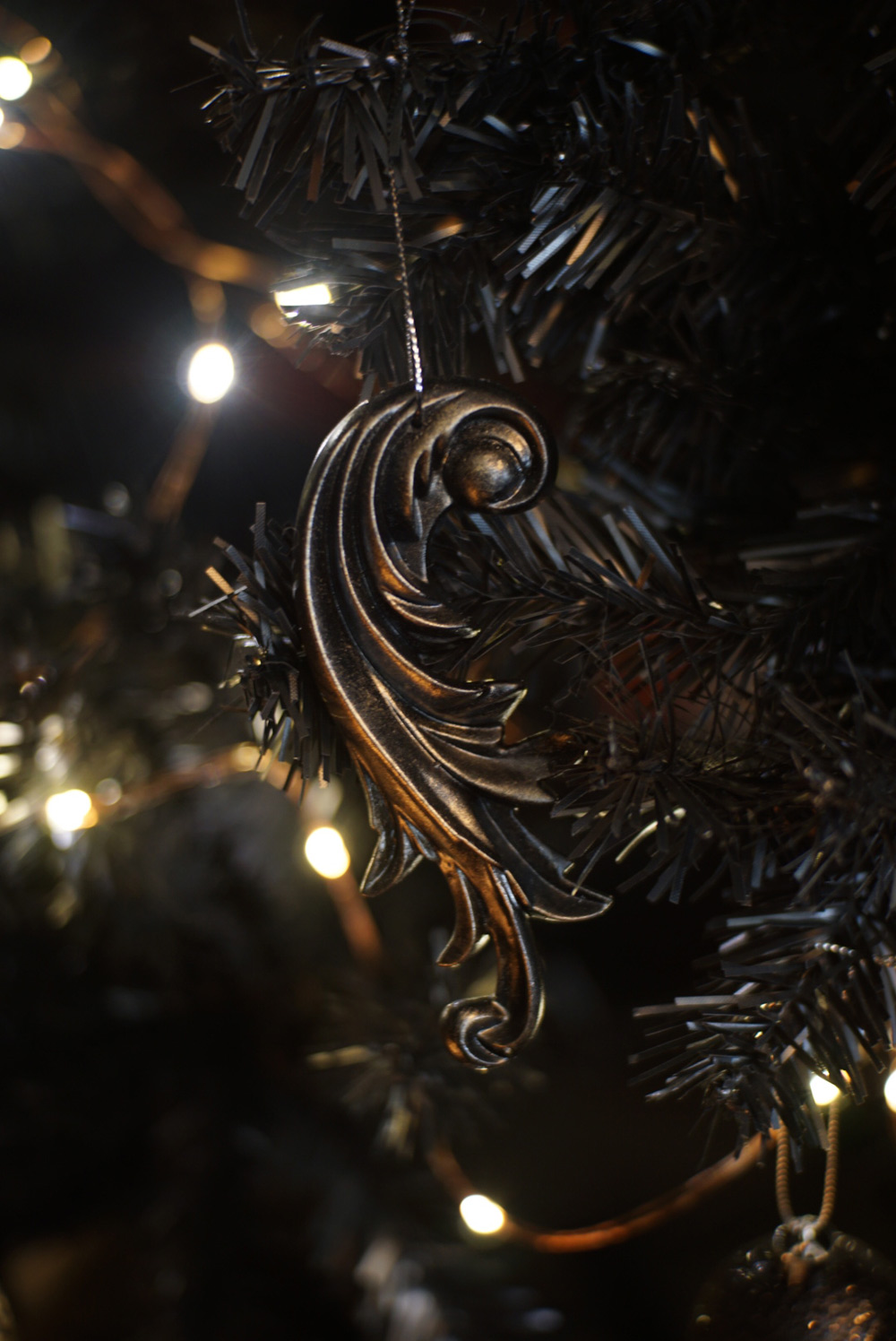 Close-up of a dark ornament hanging on a black Christmas tree with lights.