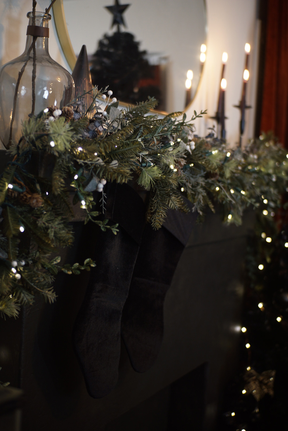A black mantel area decorated with garland, black stockings, and candles.