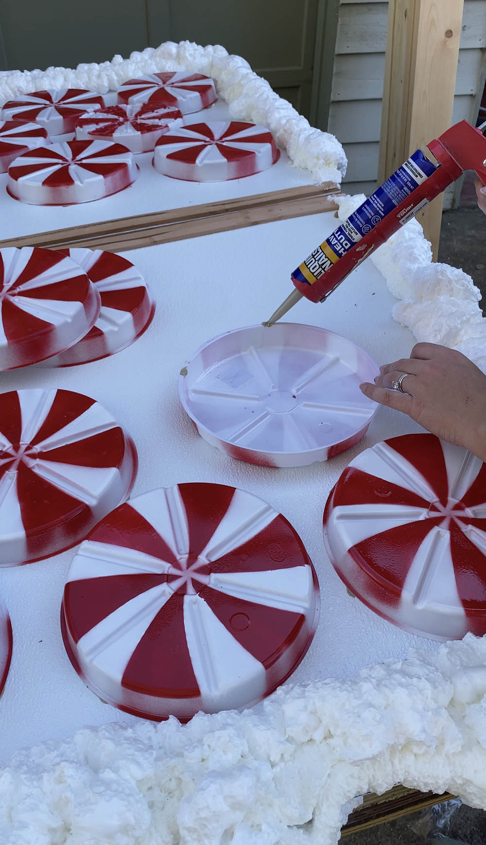 A person applying construction adhesive to the fake, oversized peppermints.