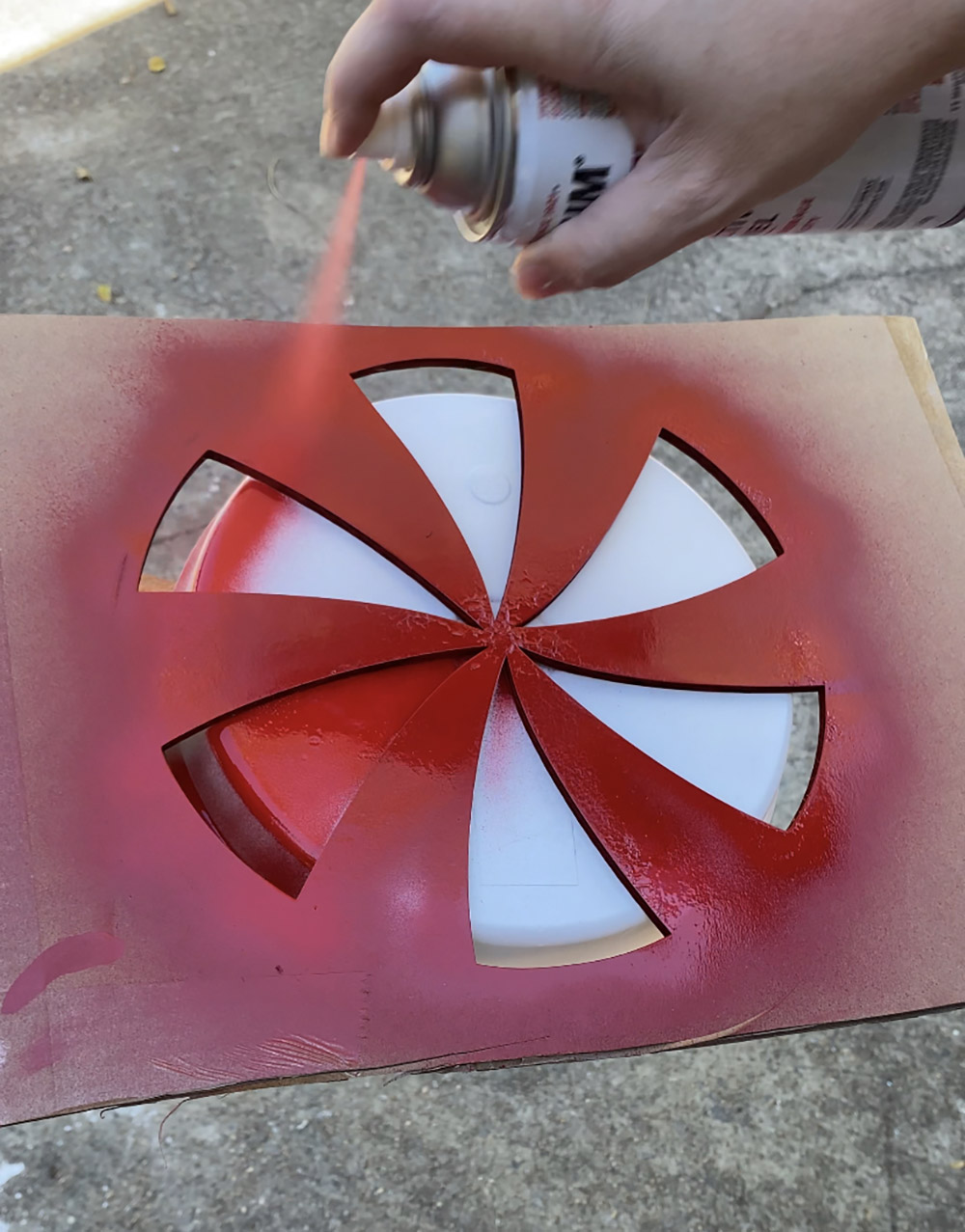 A person spray painting a peppermint stencil on a plant saucer.