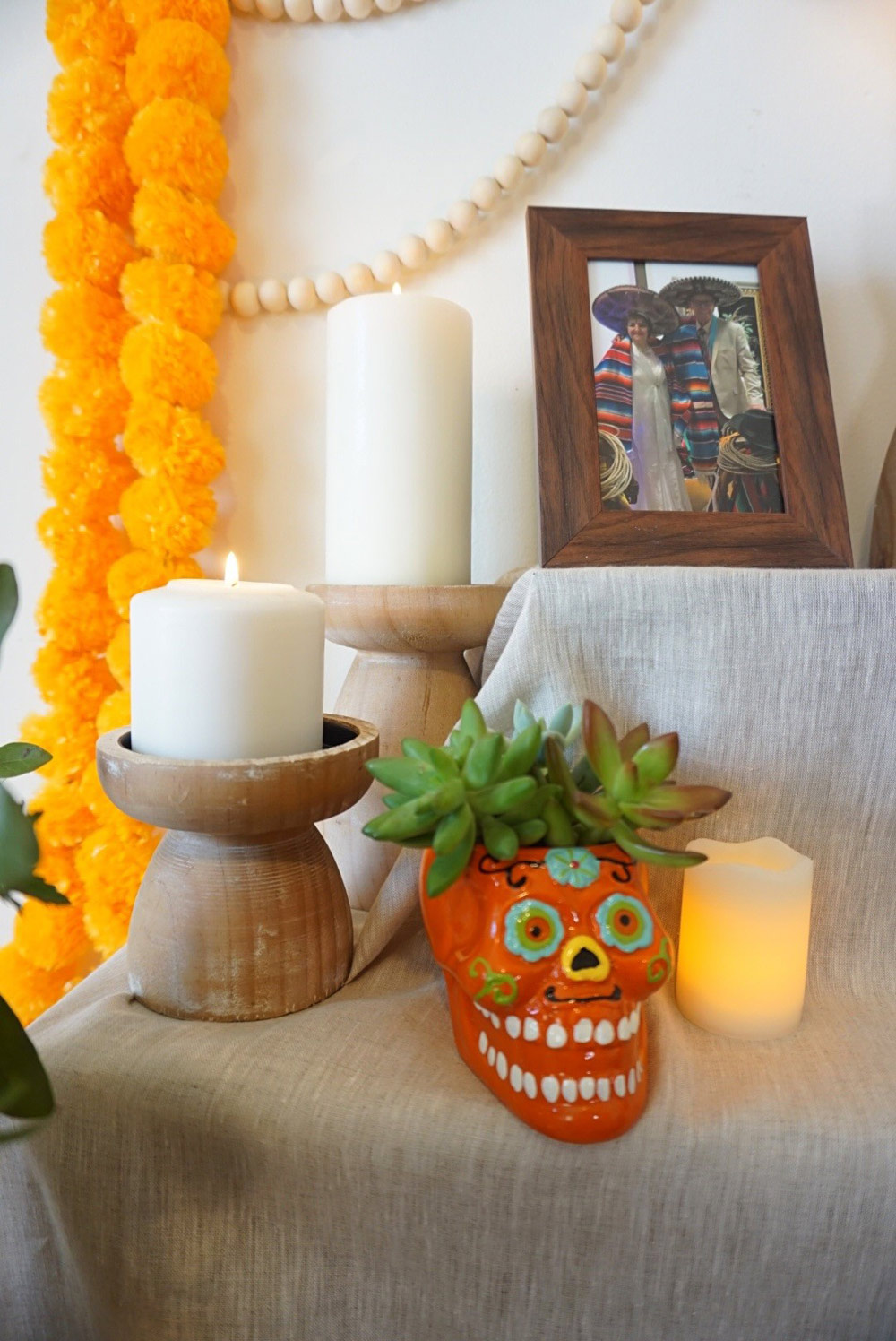 A closeup of details on Ofrenda, pictures, plants, and candles over a tablecloth.