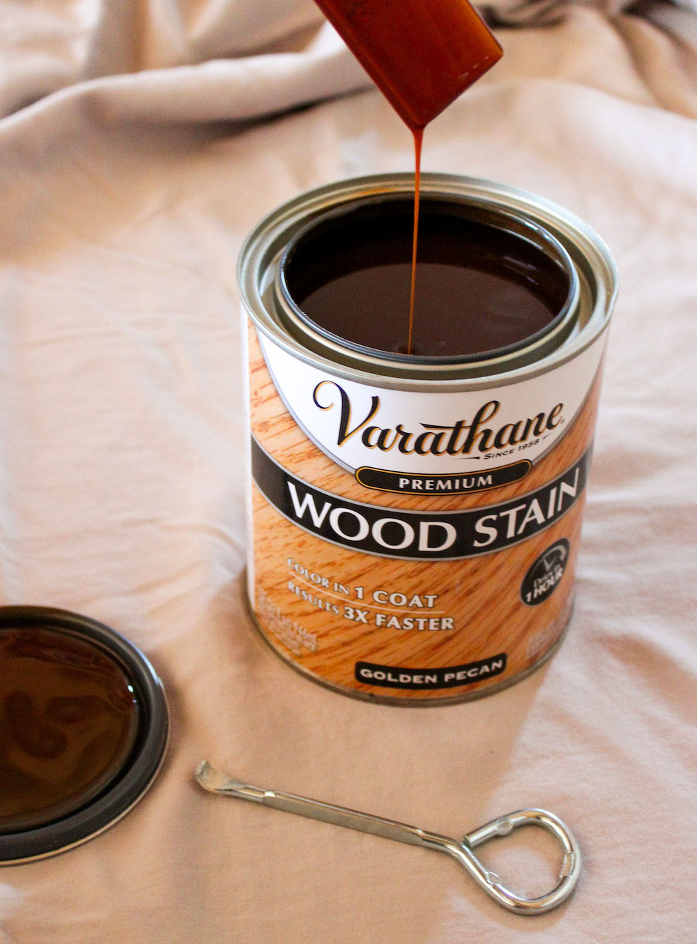 A paintbrush drips golden pecan Varathane wood stain into a can.