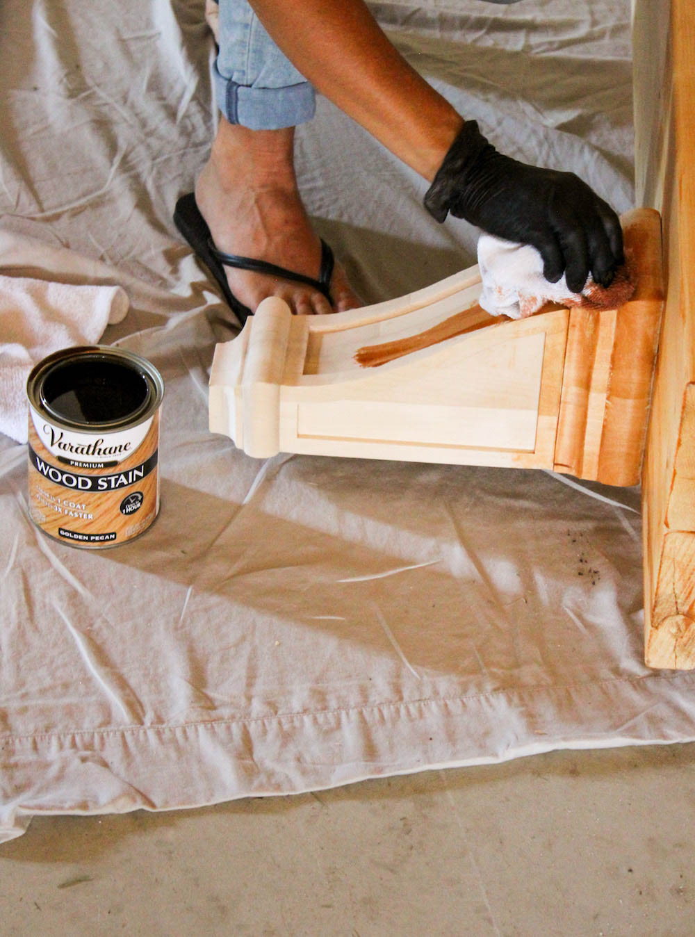 A person uses a rap to wipe Varathane premium wood stain on a wooden corbel.