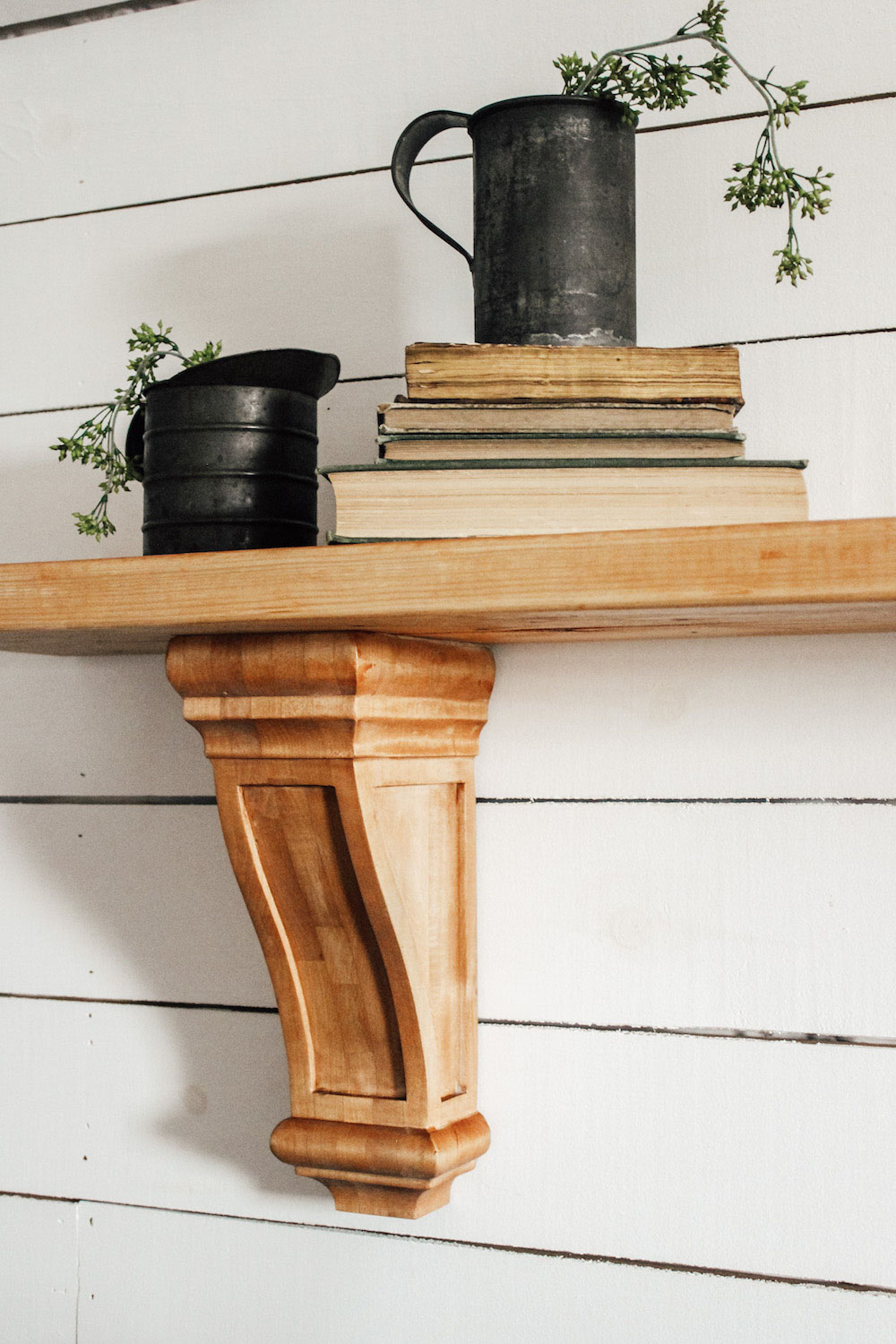 A large wooden wall shelf made with corbels is decorated with books and metal cans..