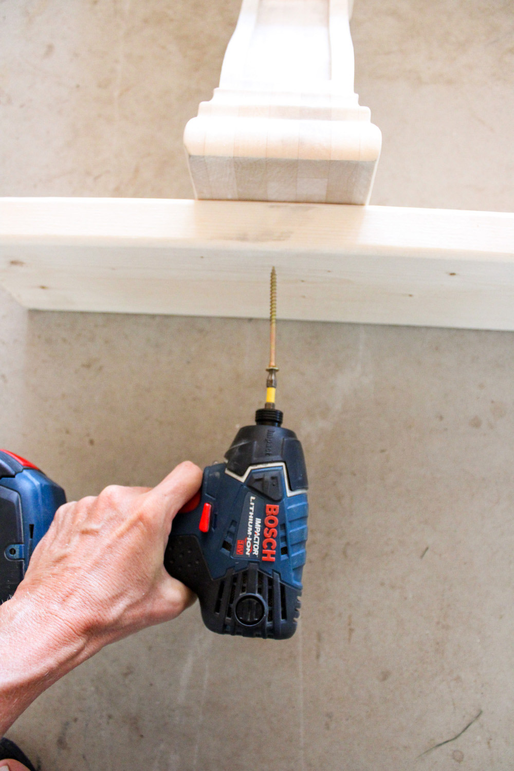 A person uses a cordless drill to attach a wood board to a corbel.