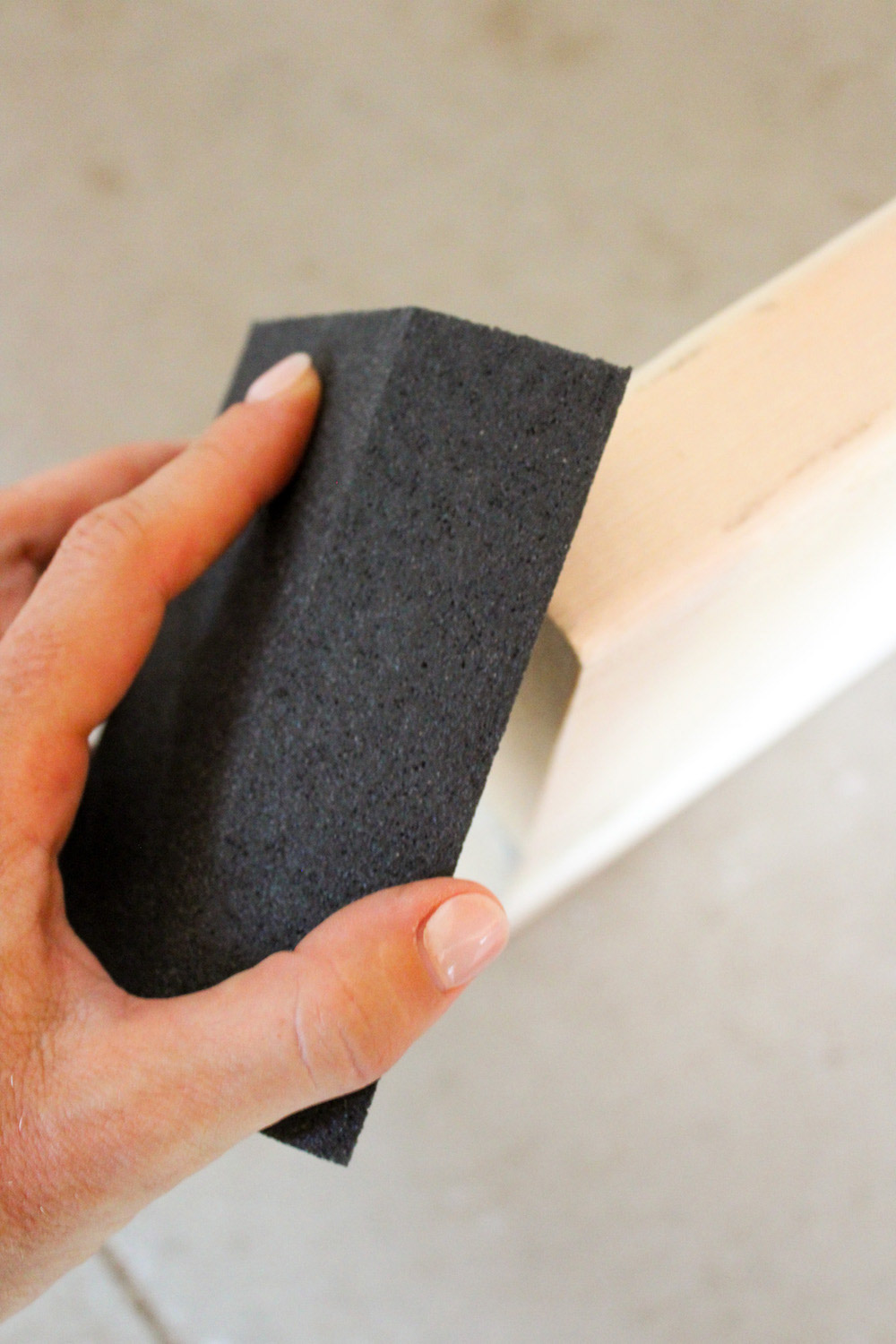 A person uses a sanding block to sand a piece of wood.