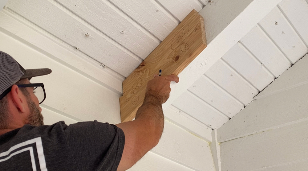 A man using a cut angle board to test the shape needed for his ceiling beams. 