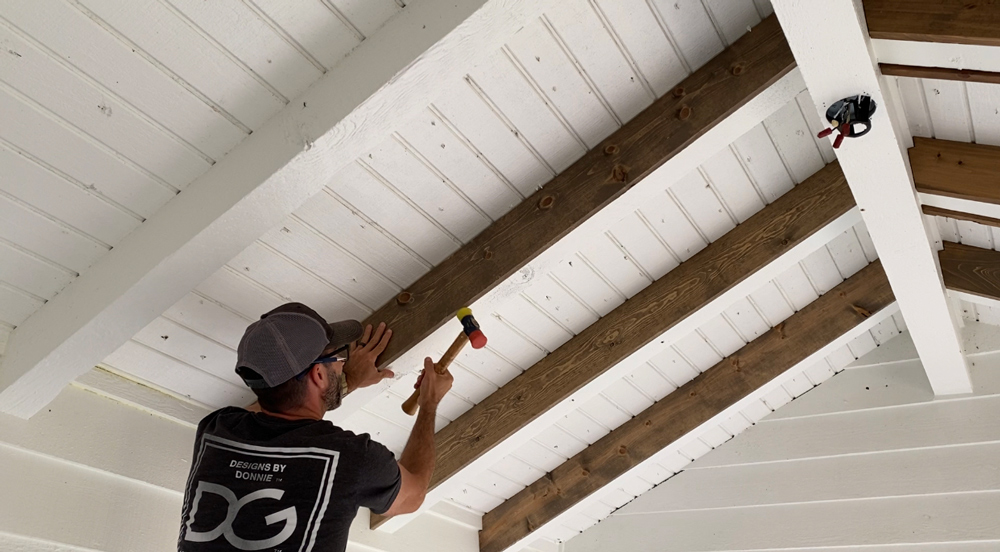 A man using a hammer to install boards into the ceiling.