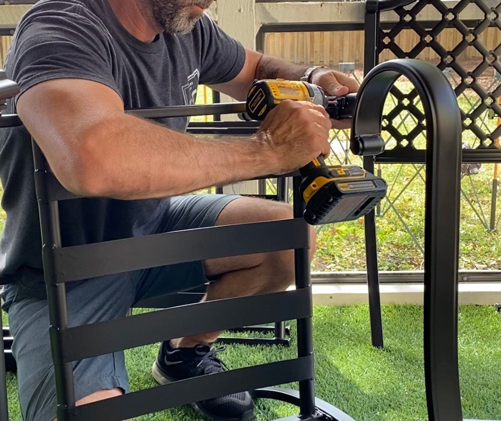 A man using a drill to secure a patio chair arm. A man using a drill to secure a patio chair arm.