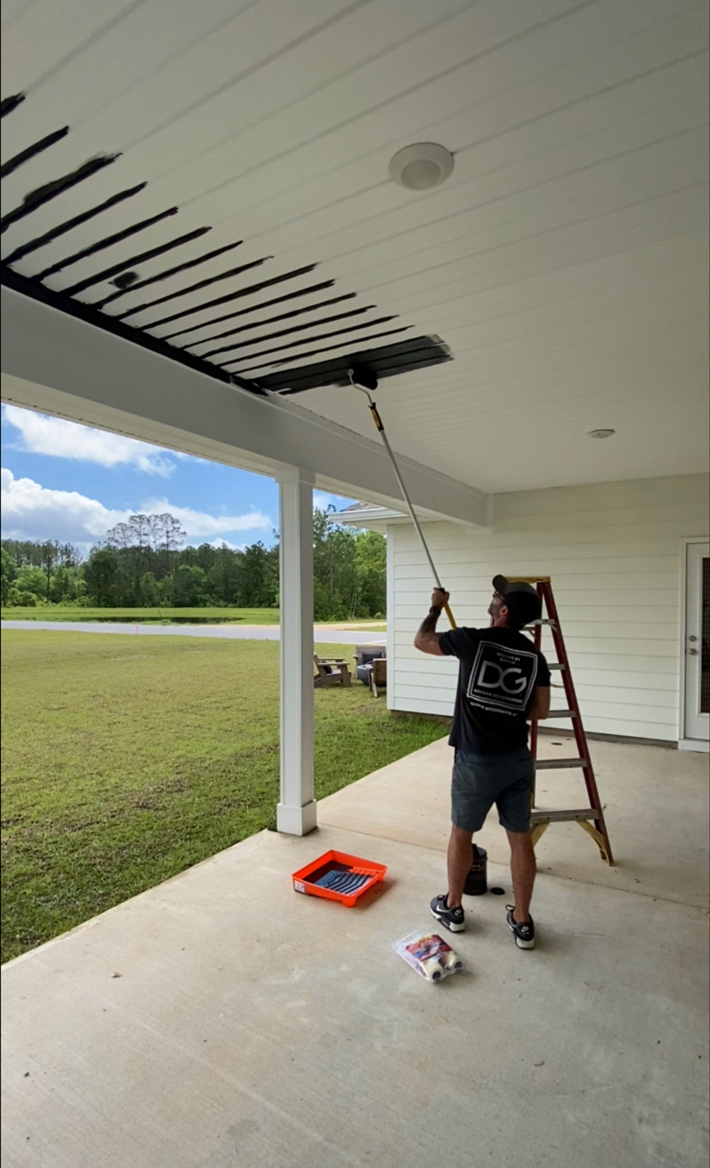 A man standing next to a ladder, painting a patio ceiling black. A man standing next to a ladder, painting a patio ceiling black.