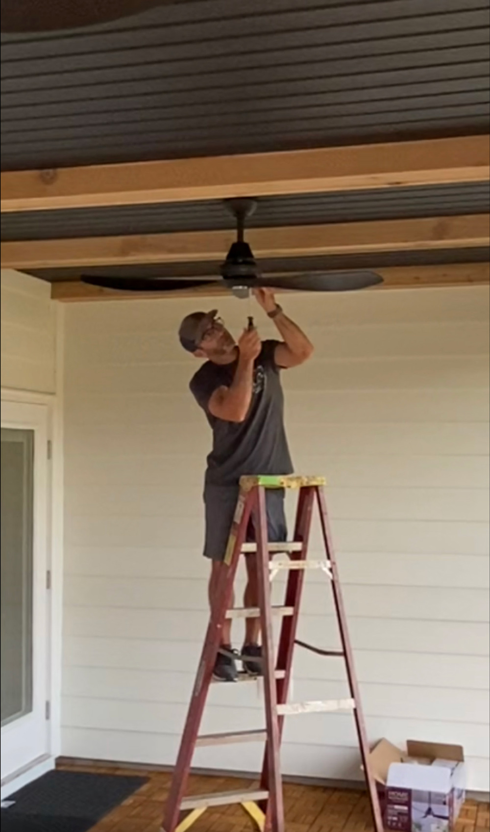 A man standing on a ladder installing a ceiling fan. A man standing on a ladder installing a ceiling fan.