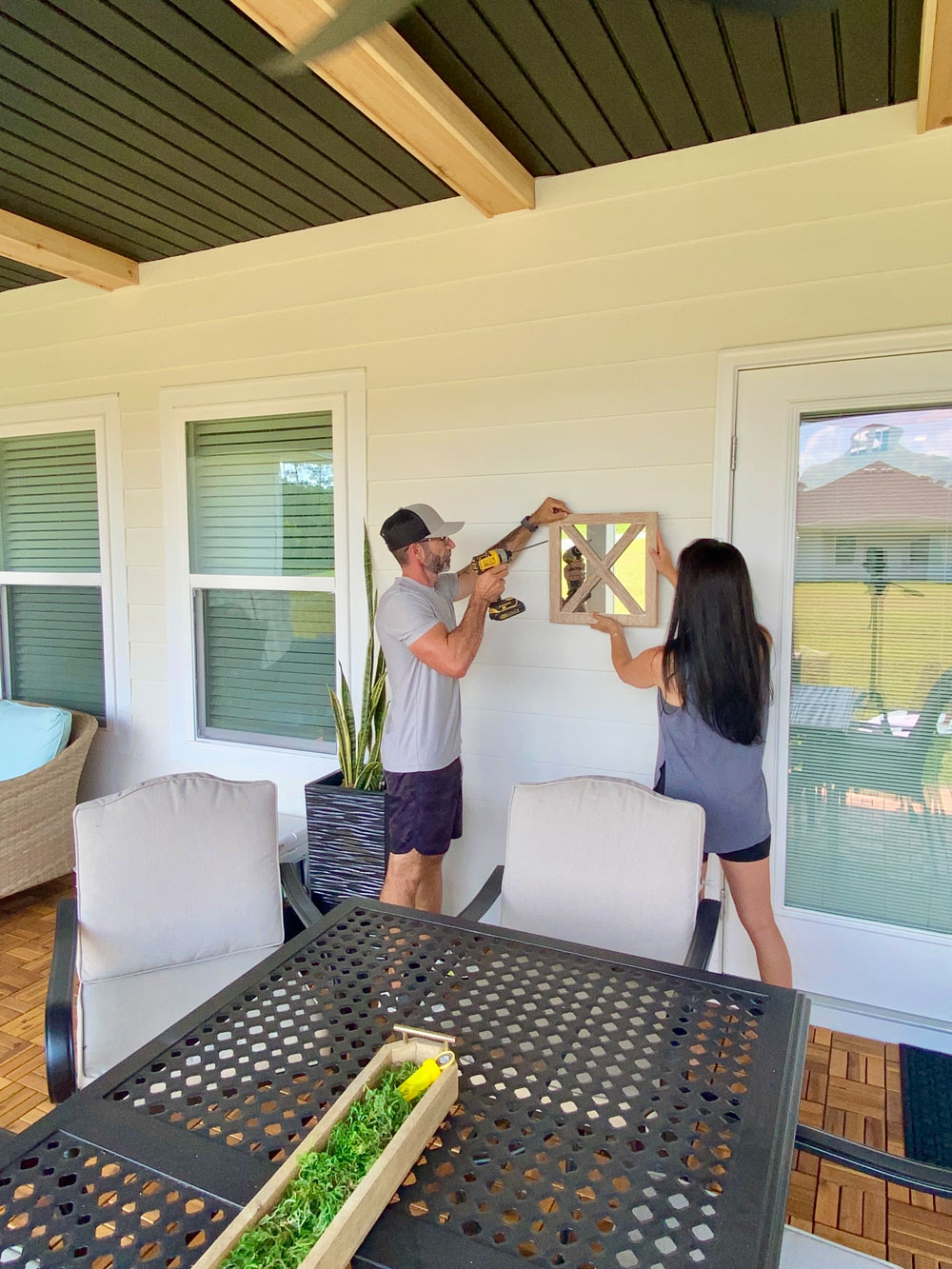 A woman holding up a mirror while the man drills the nails in to secure it into the wall. A woman holding up a mirror while the man drills the nails in to secure it into the wall.