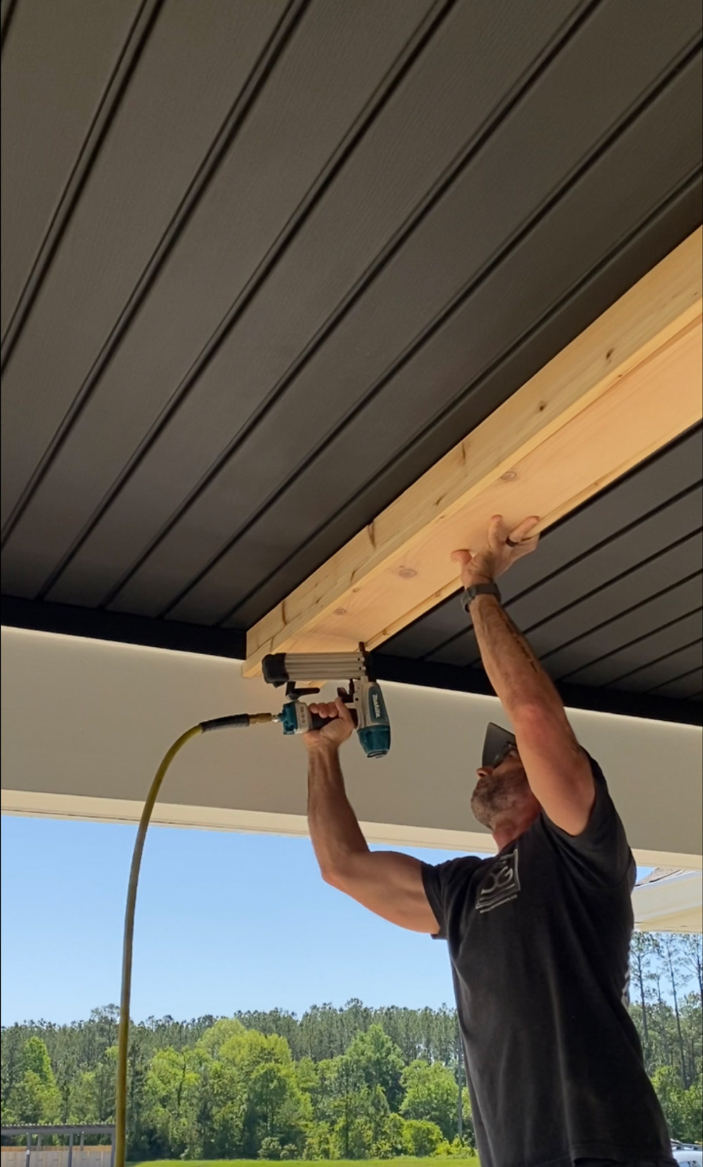 A man using a nail gun to attach cedar planks to the patio ceiling. A man using a nail gun to attach cedar planks to the patio ceiling.