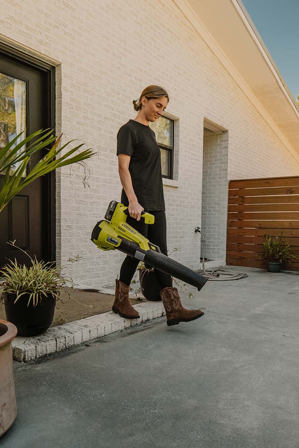 A woman using a leaf blower to clean her patio flooring. A woman using a leaf blower to clean her patio flooring.