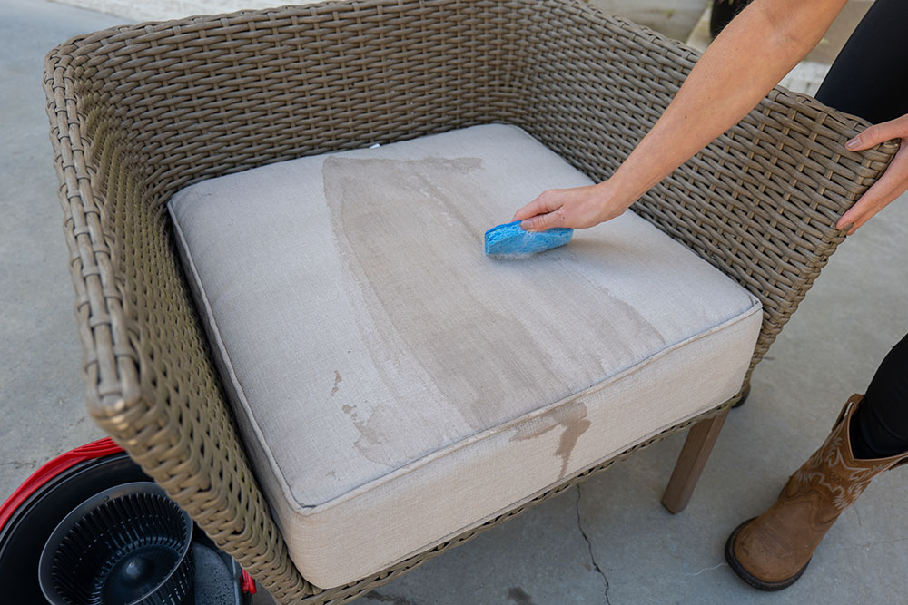 A person cleaning a sectional cushion with a sponge. A person cleaning a sectional cushion with a sponge.