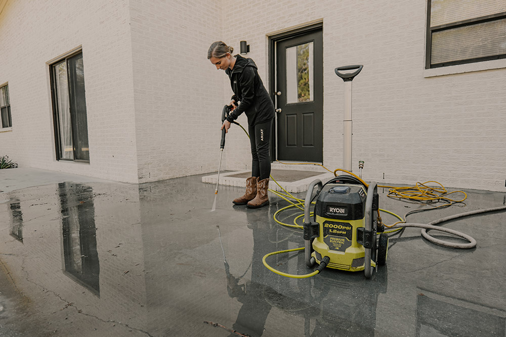 A woman using a pressure washer to clean patio flooring. A woman using a pressure washer to clean patio flooring.