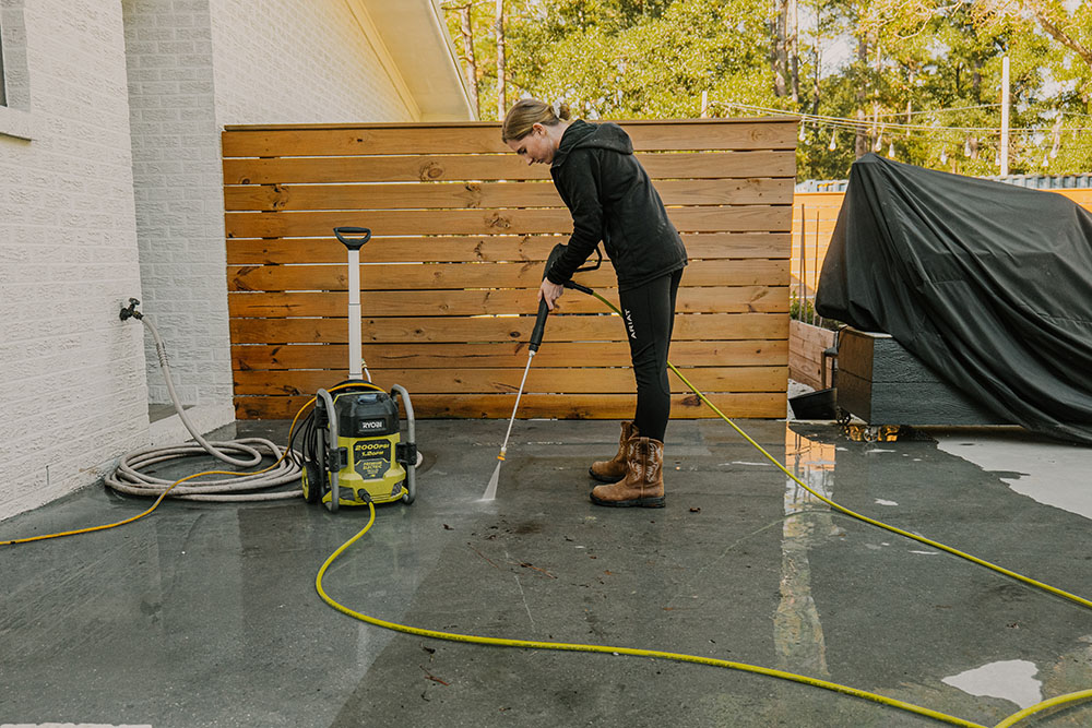 A woman using a pressure washer to clean patio flooring. A woman using a pressure washer to clean patio flooring.