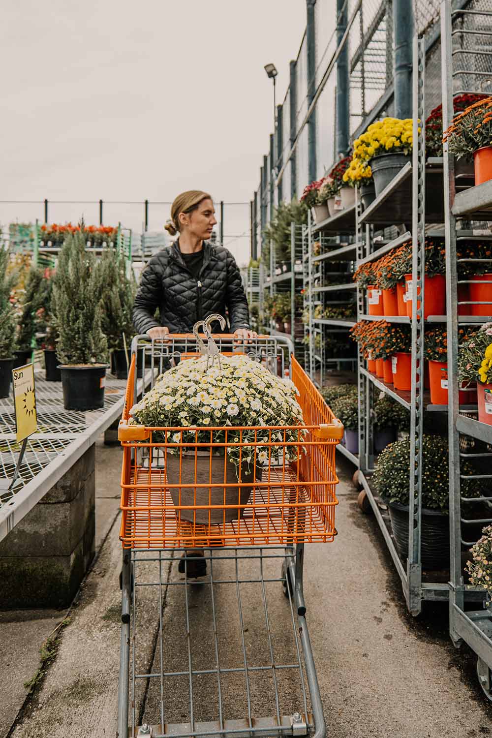 A woman walking through the garden section of The Home Depot with a shopping cart. A woman walking through the garden section of The Home Depot with a shopping cart.