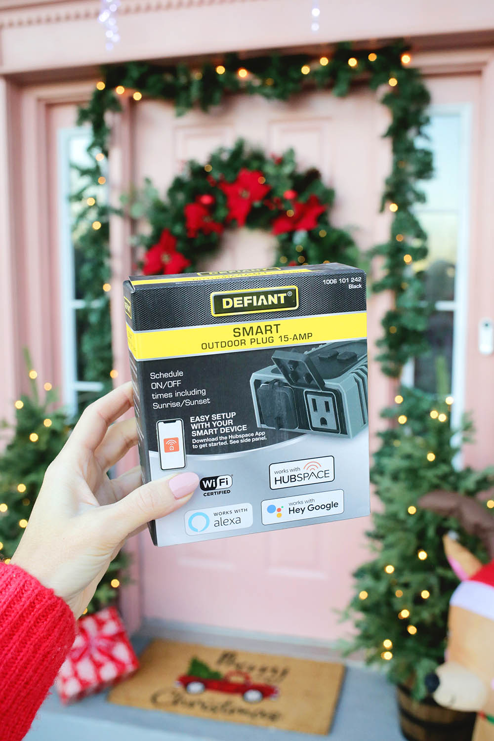 A photo of someone holding the box of a HubSpace Defiant smart plug in front of a decorated front door.